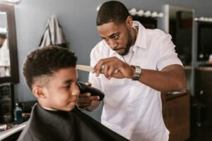 Barber in a white shirt carefully trimming a boy's hair at a salon.